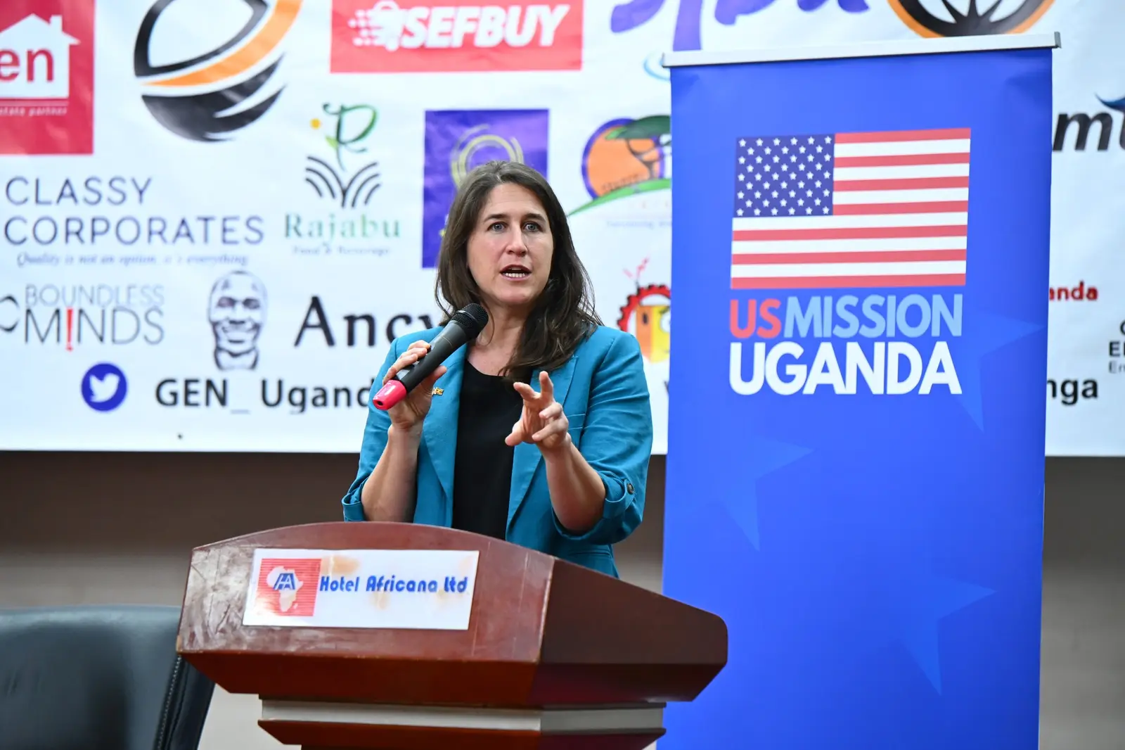 Speaker at the podium beside the US Mission Uganda banner