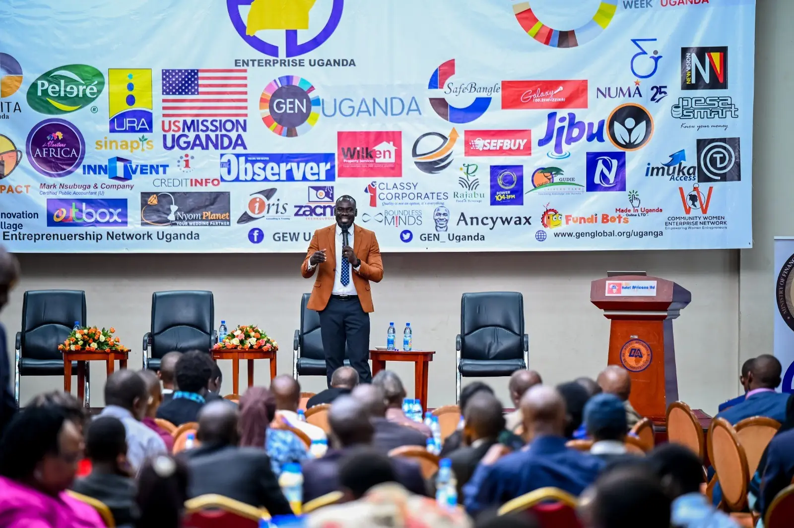 Speaker at Global Entrepreneurship Week Uganda in front of the sponsor wall